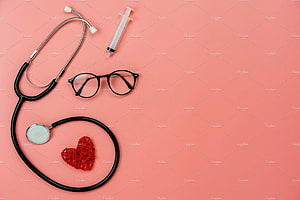 Flat lay of stethoscope, syringe, and glasses with a red heart on a pink background HD wallpaper