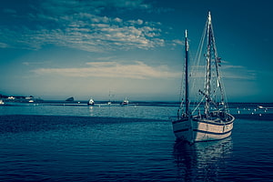 Classic Wooden Sailboat Moored in a Calm Harbor Under a Teal Sky HD wallpaper