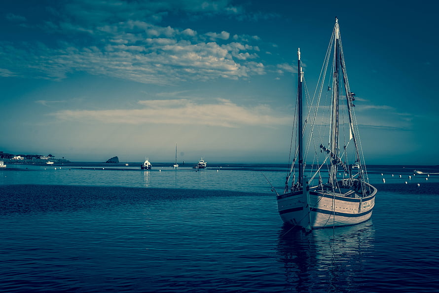 Classic Wooden Sailboat Moored in a Calm Harbor Under a Teal Sky HD wallpaper