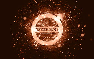 Volvo emblem glowing with warm amber light and floating particles on a dark abstract background HD wallpaper