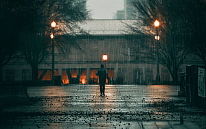 Solitary figure walking through a rainy city plaza at dusk with glowing street lamps HD wallpaper