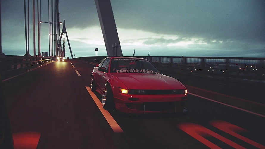 Red Nissan Skyline R32 drifting on a suspension bridge at dusk with headlights on HD wallpaper