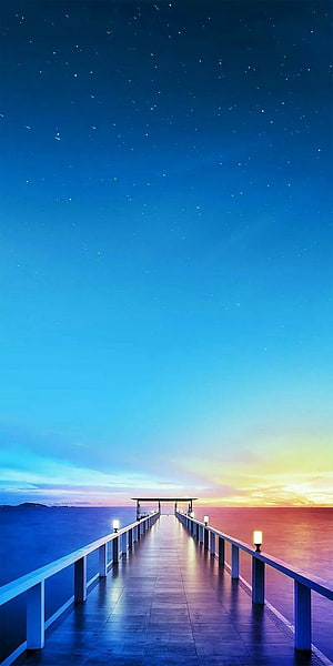 Illuminated pier extending into the ocean under a starry twilight sky HD phone wallpaper