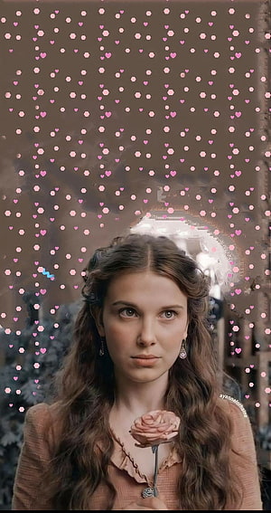 Millie Bobby Brown in vintage attire holding a rose with soft pink heart overlay HD phone wallpaper