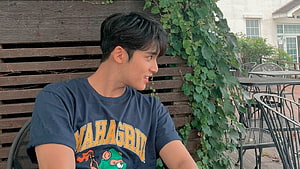 Mingyu from Seventeen in a navy graphic tee at an outdoor cafe with ivy-covered wooden wall HD wallpaper