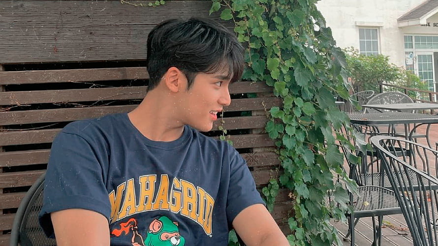 Mingyu from Seventeen in a navy graphic tee at an outdoor cafe with ivy-covered wooden wall HD wallpaper
