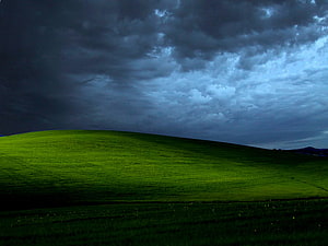 Dramatic Storm Clouds Over a Lush Green Rolling Hill at Dusk HD wallpaper
