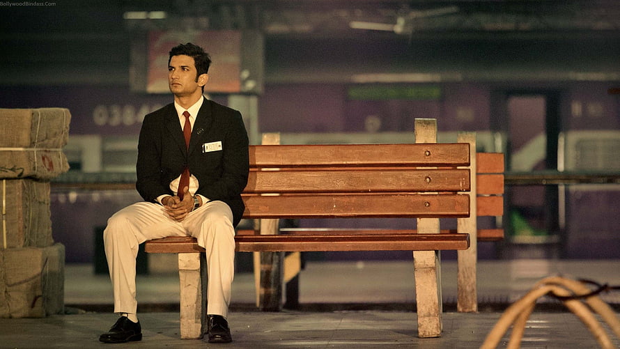 Sushant Singh Rajput in M.S. Dhoni: The Untold Story sitting on a wooden bench at a train station HD wallpaper