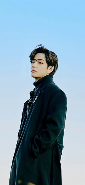 Kim Taehyung in a dark winter coat against a clear blue sky HD phone wallpaper