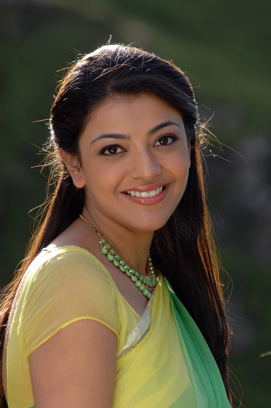 Kajal Agarwal in a yellow and green sari with a beaded necklace, smiling outdoors HD phone wallpaper