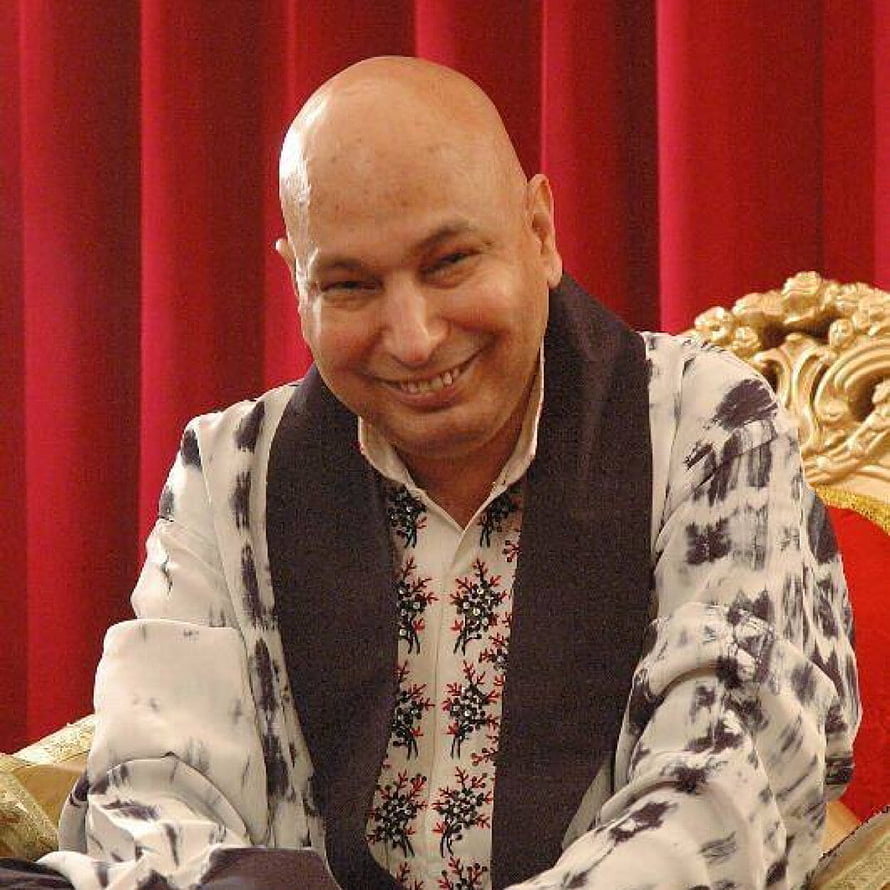 Portrait of a smiling bald man in traditional embroidered attire seated before a red curtain, Guruji Chatarpur - Guruji Bade Mandir Timings - - teahub.io HD phone wallpaper