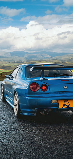 Blue Nissan Skyline GT-R R34 Rear View on Mountain Road with Dramatic Sky HD phone wallpaper