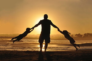 Silhouette of a father spinning two children on a beach at golden hour sunset HD wallpaper