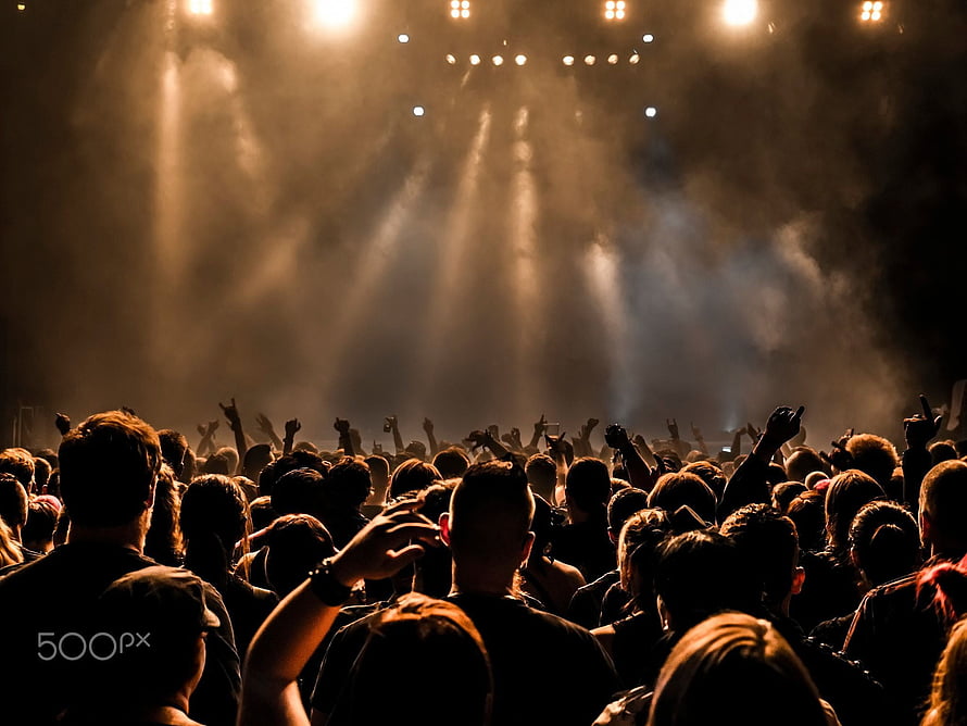 Silhouetted concert crowd with raised hands beneath dramatic golden stage lighting and atmospheric haze HD wallpaper