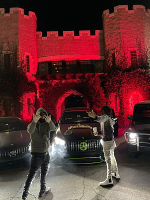 YEAT posing with a customized Mercedes AMG in front of a red-lit castle at night HD phone wallpaper