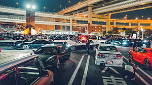 Nighttime car meet at Daikoku PA with classic and modern sports cars under highway overpass HD wallpaper