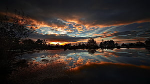 Dramatic Sunset Over a Calm Lake with Vivid Cloud Reflections and Silhouetted Trees HD wallpaper