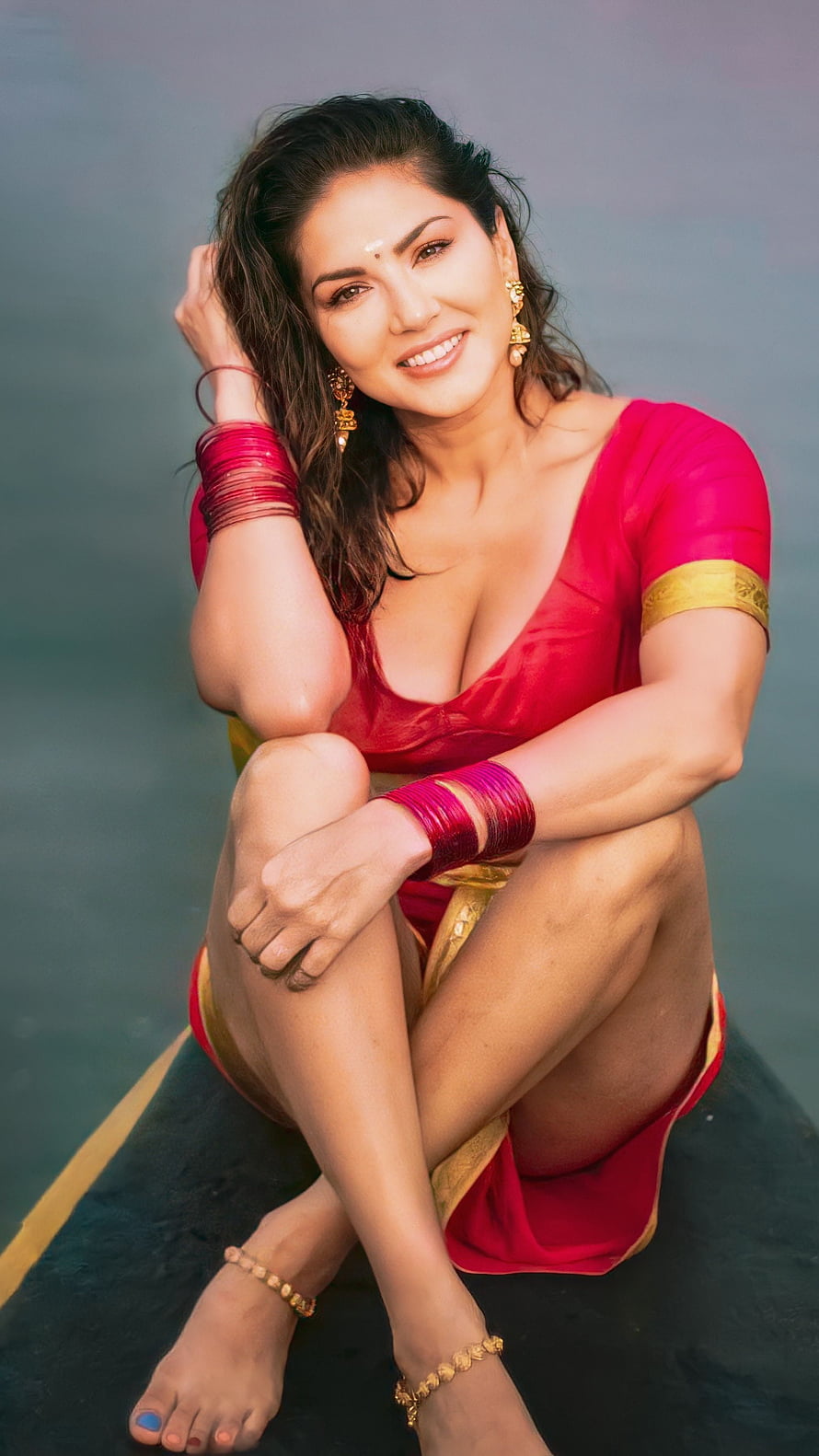 Sunny Leone in a vibrant red saree with gold trim, seated gracefully with traditional bangles and jewelry HD phone wallpaper