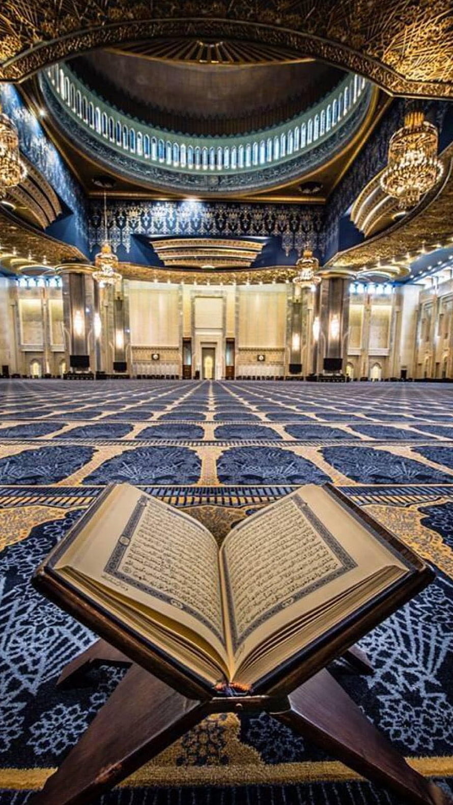 Open Quran on a wooden stand inside a grand mosque with ornate golden dome and patterned carpet HD phone wallpaper