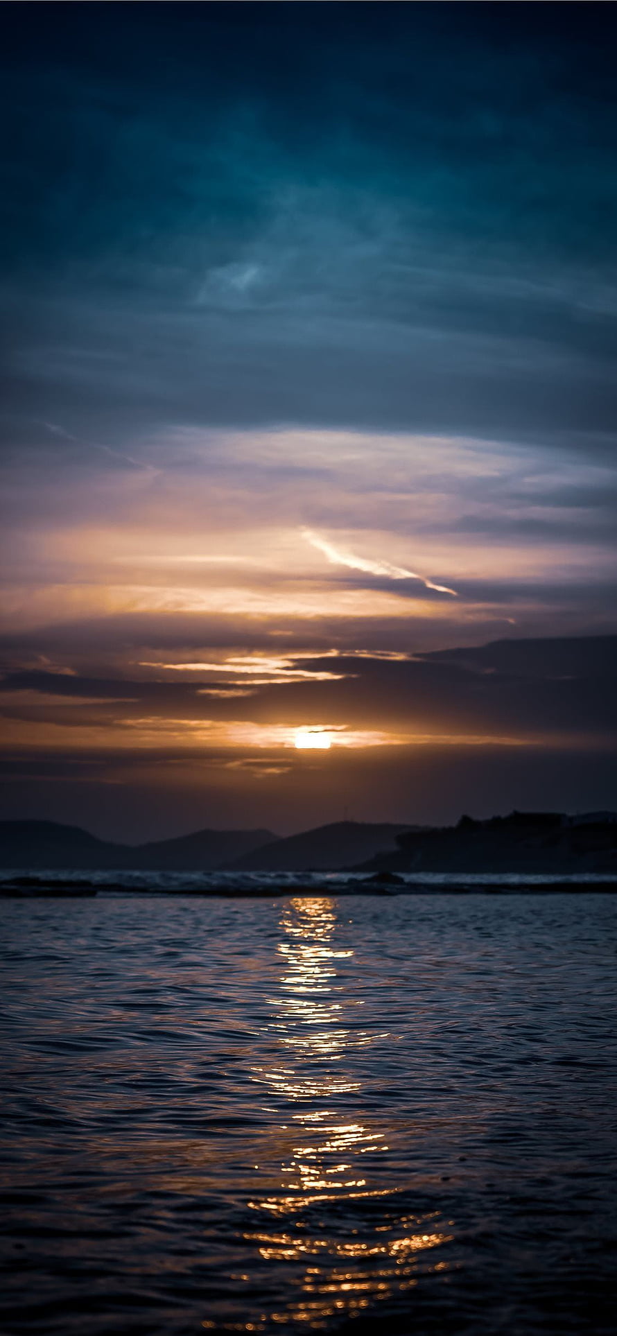 Golden sunset over calm ocean waters with distant hills and dramatic clouds HD phone wallpaper