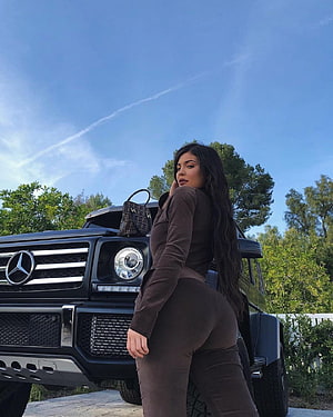 Kylie Jenner posing in a brown outfit beside a black Mercedes G-Class SUV under a clear blue sky HD phone wallpaper