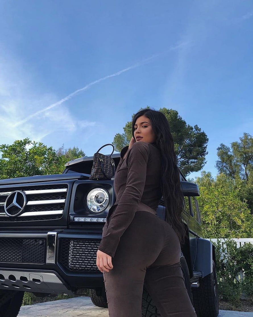 Kylie Jenner posing in a brown outfit beside a black Mercedes G-Class SUV under a clear blue sky HD phone wallpaper