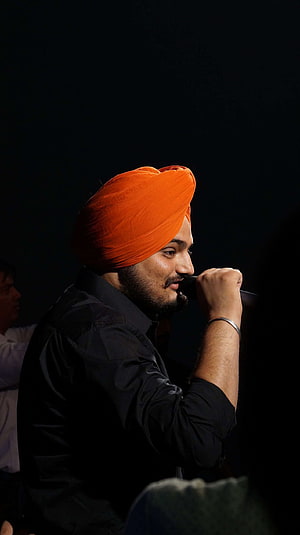 Sidhu Moosewala performing live on stage wearing a vibrant orange turban and black shirt HD phone wallpaper