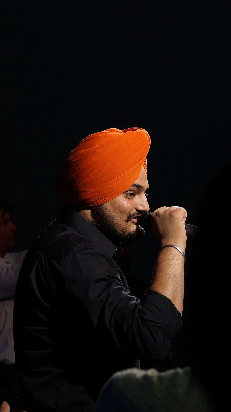 Sidhu Moosewala performing live on stage wearing a vibrant orange turban and black shirt HD phone wallpaper