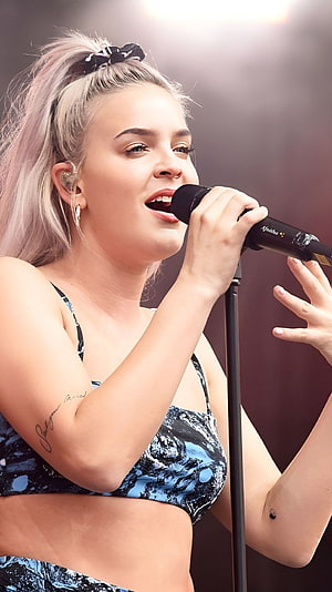 Anne Marie performing live on stage with microphone and blonde ponytail HD phone wallpaper