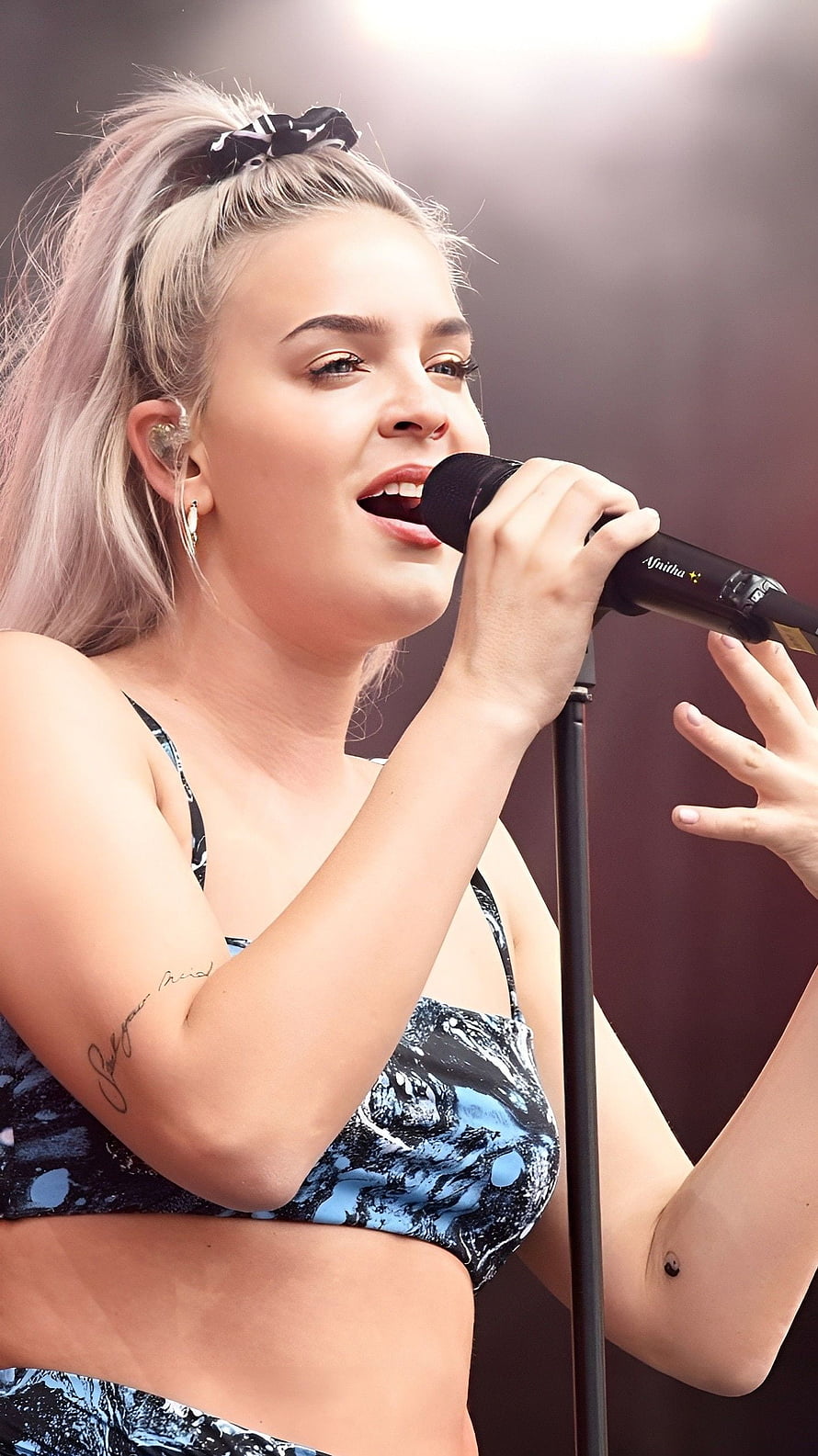 Anne Marie performing live on stage with microphone and blonde ponytail HD phone wallpaper