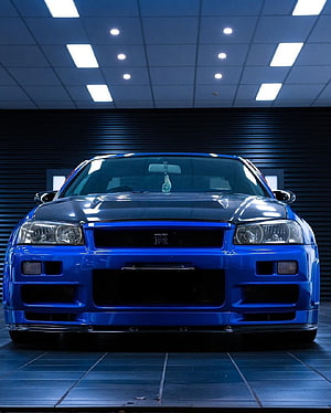 Front View of a Blue Nissan Skyline R34 GTR in a Modern Showroom Setting HD phone wallpaper