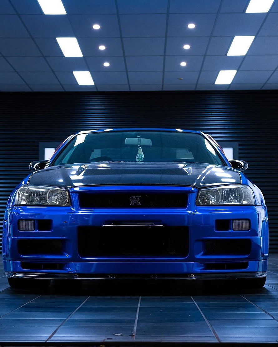 Front View of a Blue Nissan Skyline R34 GTR in a Modern Showroom Setting HD phone wallpaper