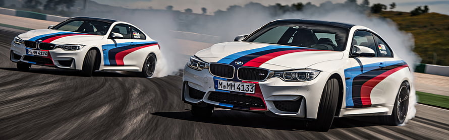 Two BMW M4 Coupes Drifting on a Race Track with Tire Smoke and Motion Blur HD wallpaper