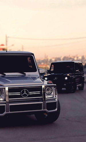 Silver and Black Mercedes-Benz G-Class SUVs Driving on a City Road at Sunset HD phone wallpaper