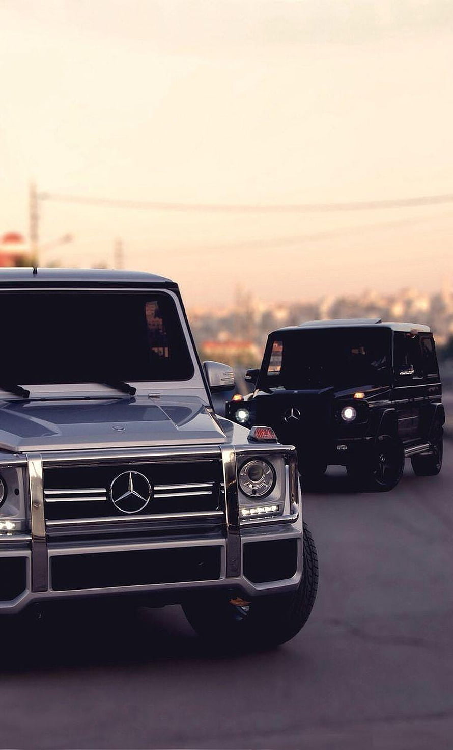 Silver and Black Mercedes-Benz G-Class SUVs Driving on a City Road at Sunset HD phone wallpaper