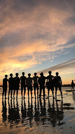 Group of friends silhouetted on a wet beach at sunset with reflections in the water HD phone wallpaper