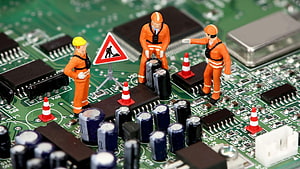 Miniature construction workers repairing a green circuit board with traffic cones and warning signs HD wallpaper