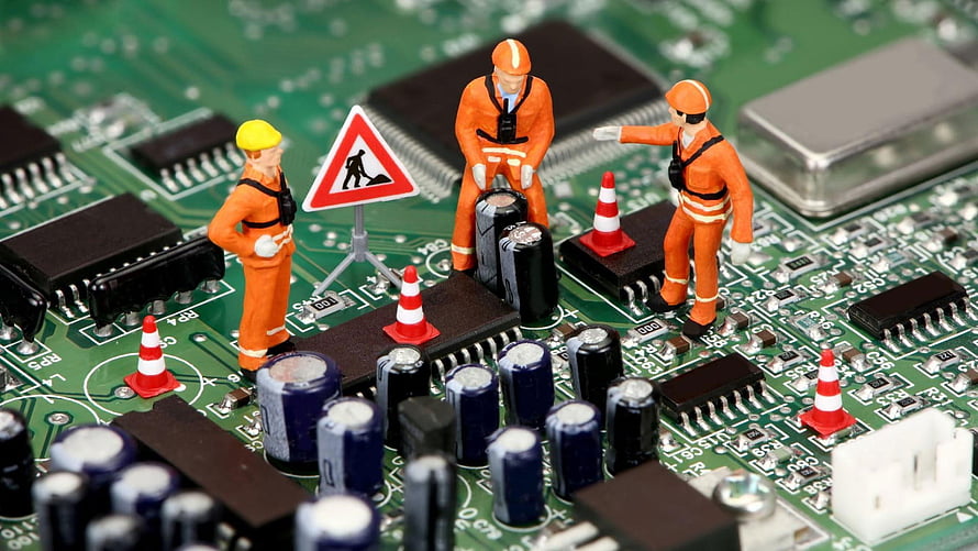 Miniature construction workers repairing a green circuit board with traffic cones and warning signs HD wallpaper