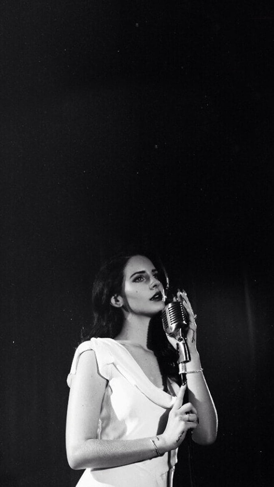 Lana Del Rey in a white dress singing into a vintage microphone on a dark stage HD phone wallpaper