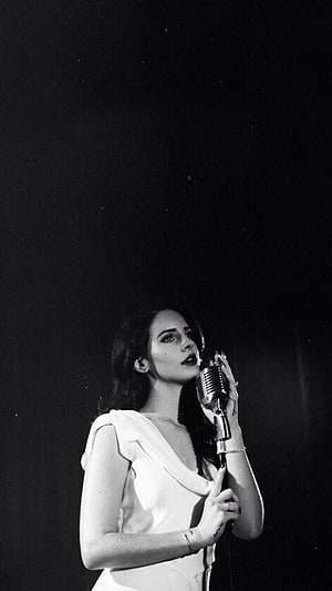 Lana Del Rey performing with vintage microphone in dramatic black and white portrait HD phone wallpaper