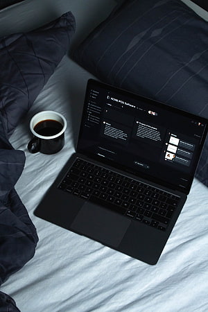 Black laptop and coffee mug on a bed with dark bedding HD phone wallpaper