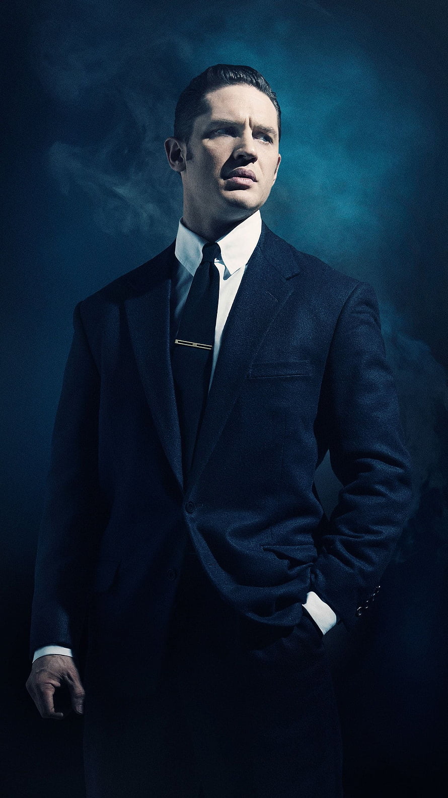 Tom Hardy in a dark navy suit with a black tie against a moody blue smoky background HD phone wallpaper