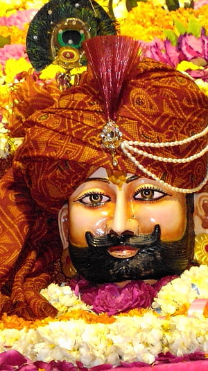 Khatu Shyam deity adorned in ornate turban and peacock feather amidst vibrant flower garlands HD phone wallpaper