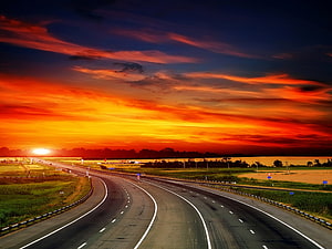 Vibrant sunset over a curving highway with dramatic orange and red clouds in the sky HD wallpaper