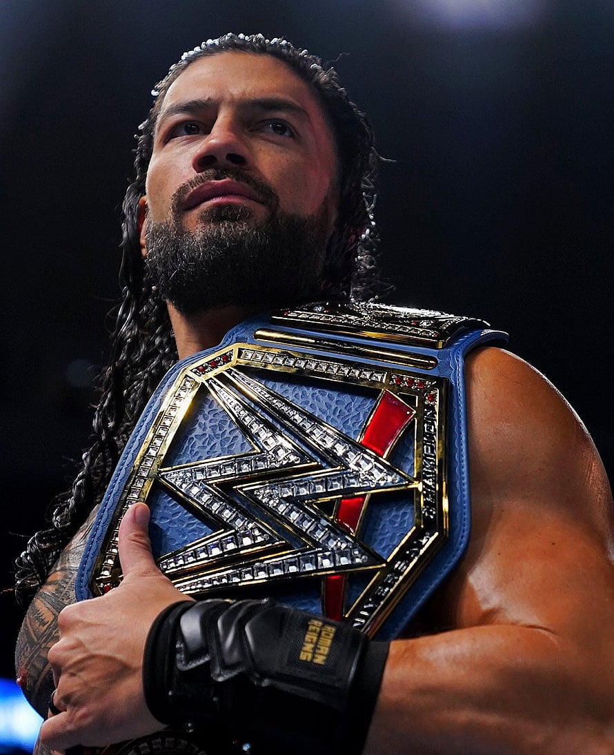 Roman Reigns Holding The WWE Universal Championship Belt In A Dramatic Arena Setting HD phone wallpaper