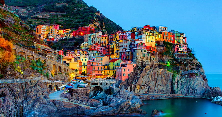 Colorful cliffside village in Italy at dusk with Mediterranean coastline and rocky shoreline HD wallpaper
