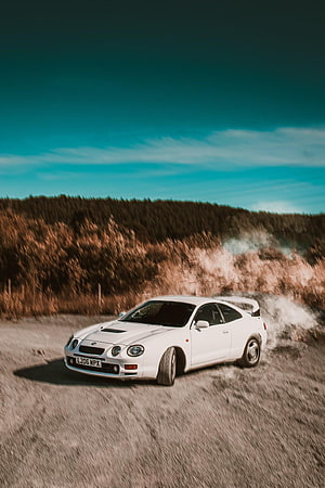 White Toyota Celica GT Four drifting on a gravel road with smoke and a forest backdrop HD phone wallpaper