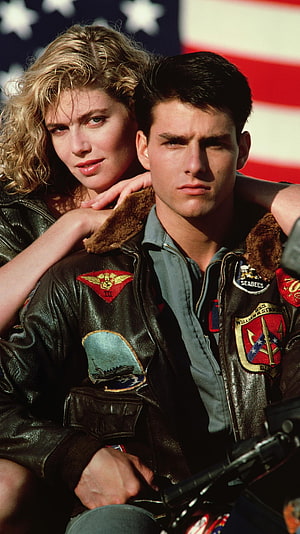Tom Cruise and Kelly McGillis in Top Gun leather flight jackets with American flag backdrop HD phone wallpaper