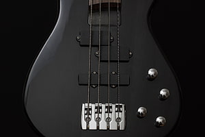 Close-up of a black electric bass guitar body with chrome hardware and strings HD wallpaper