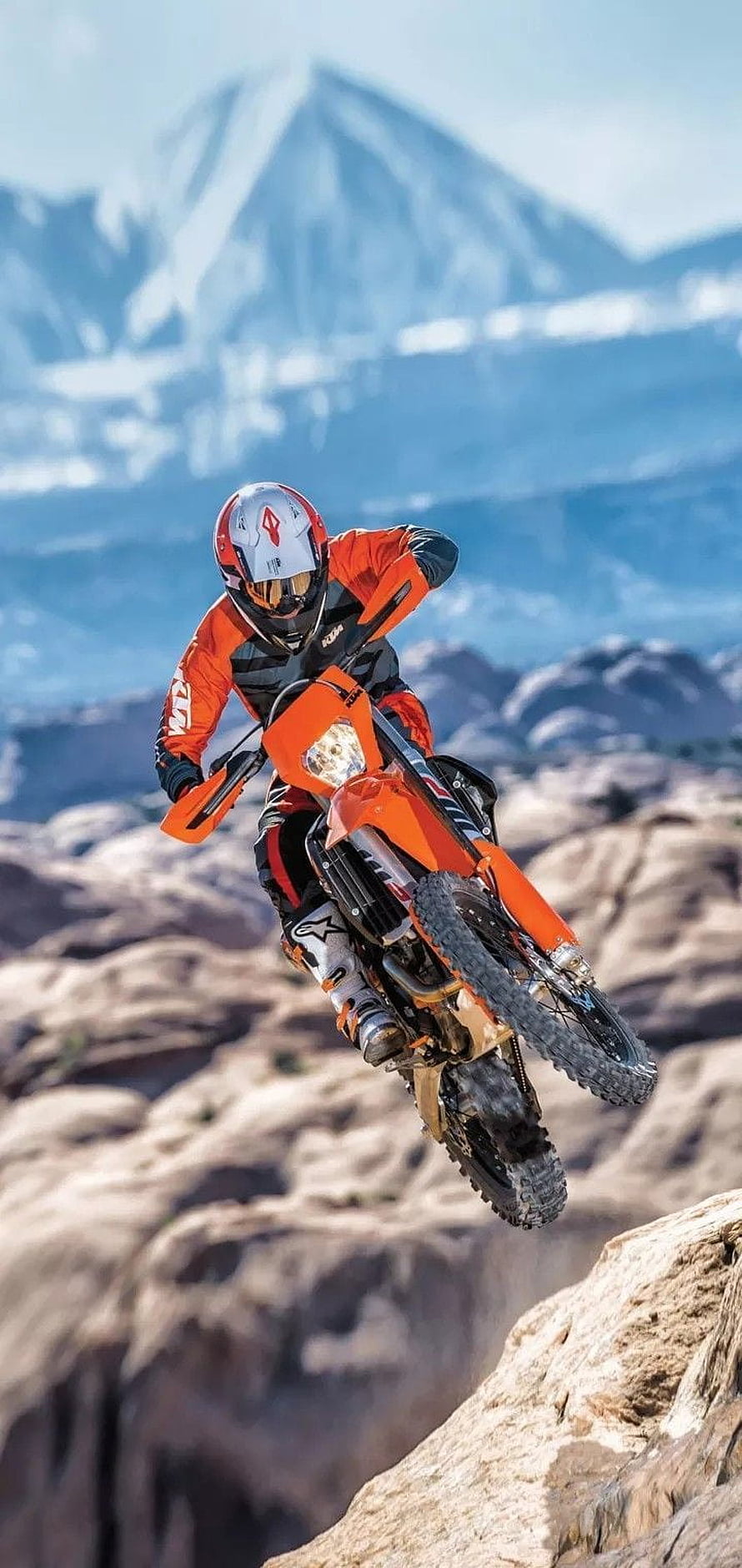 KTM Enduro Rider Launching Off Rocky Cliff With Snow-Capped Mountain Backdrop HD phone wallpaper